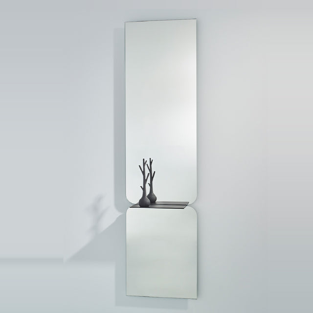 Taille full length hall mirror, 180cm, frameless rectangular glass in two panes with rounded join and black metal shelf, shown on a plain light grey wall.