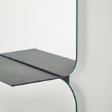 Close-up of the Taille full length hall mirror, showing two frameless rectangular glass panes with rounded corners meeting at a folded black metal shelf, against a plain white wall.