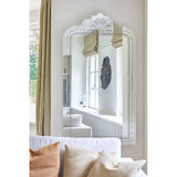 Haussmann full length mirror with scrolled crest and moulded frame, reflecting a light neutral living room with curtains, artwork, and a sofa with cushions.