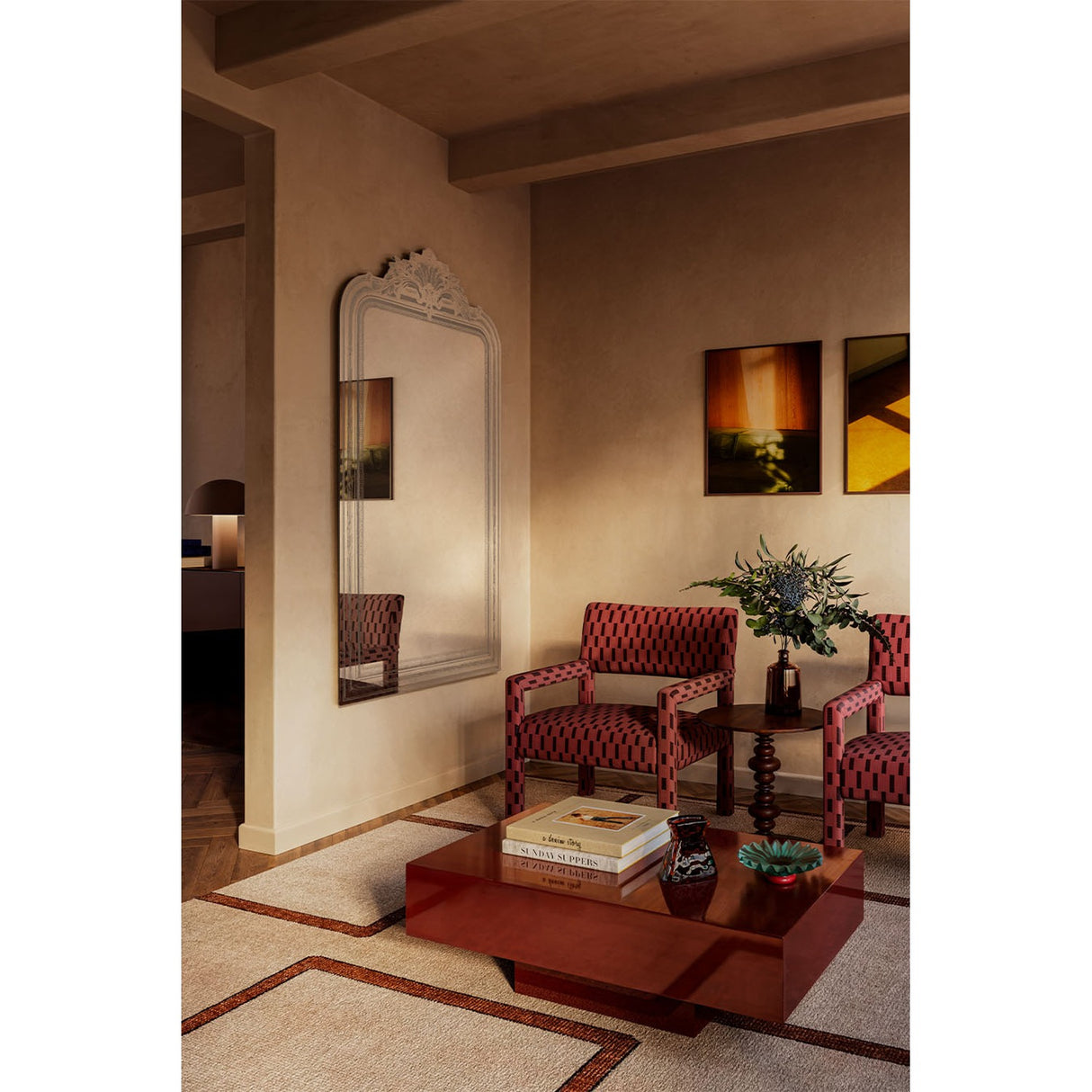 Haussmann full length mirror with arched, crested frame in a light finish, leaning against a living room wall beside red patterned armchairs and a dark wood coffee table.