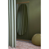 Obu Organic Full Length Leaning Mirror 178cm in gold, with an organic rock-shaped reflective area on clear glass, leaning against an olive green wall beside a sage curtain.