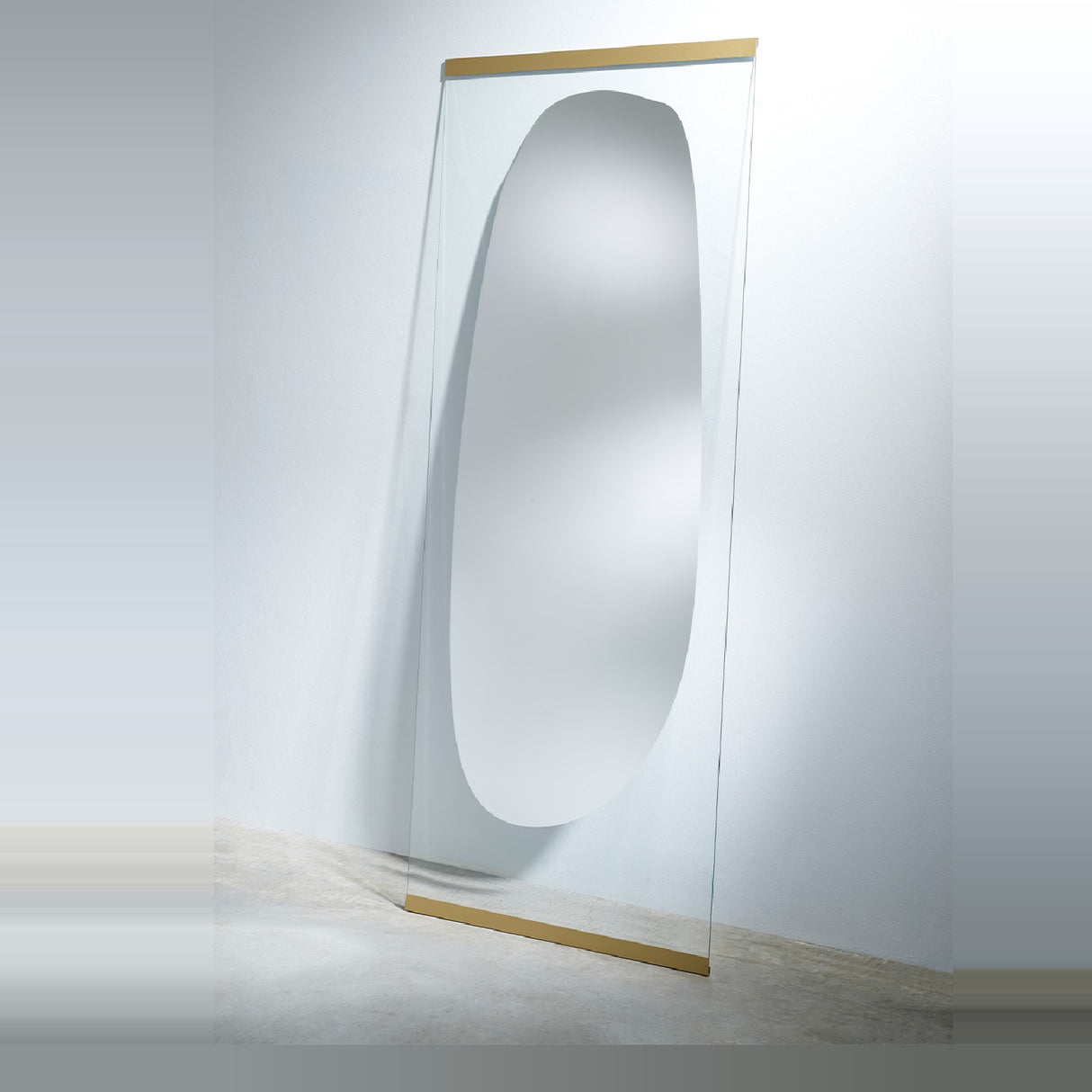The leaning mirror seen from the side, standing on the floor at a slight angle with the clear glass edge catching the light.