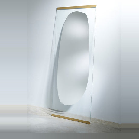 The leaning mirror seen from the side, standing on the floor at a slight angle with the clear glass edge catching the light.