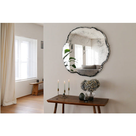 Arbo Dark irregular frameless wall mirror with printed timber-effect glass, shown above a wooden console table with candles and vases in a living room.