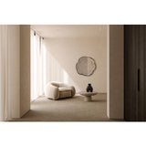 Arbo Dark Irregular Printed Glass Wall Mirror with a frameless, tree-ring inspired shape in dark tones, mounted above a bouclé armchair in a neutral living room.