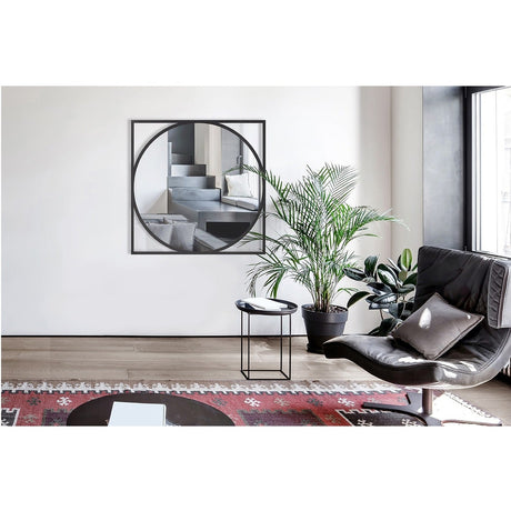 Circo Square Printed Glass Wall Mirror with black square frame and circular mirrored centre, shown hanging in a living room above a side table and armchair.