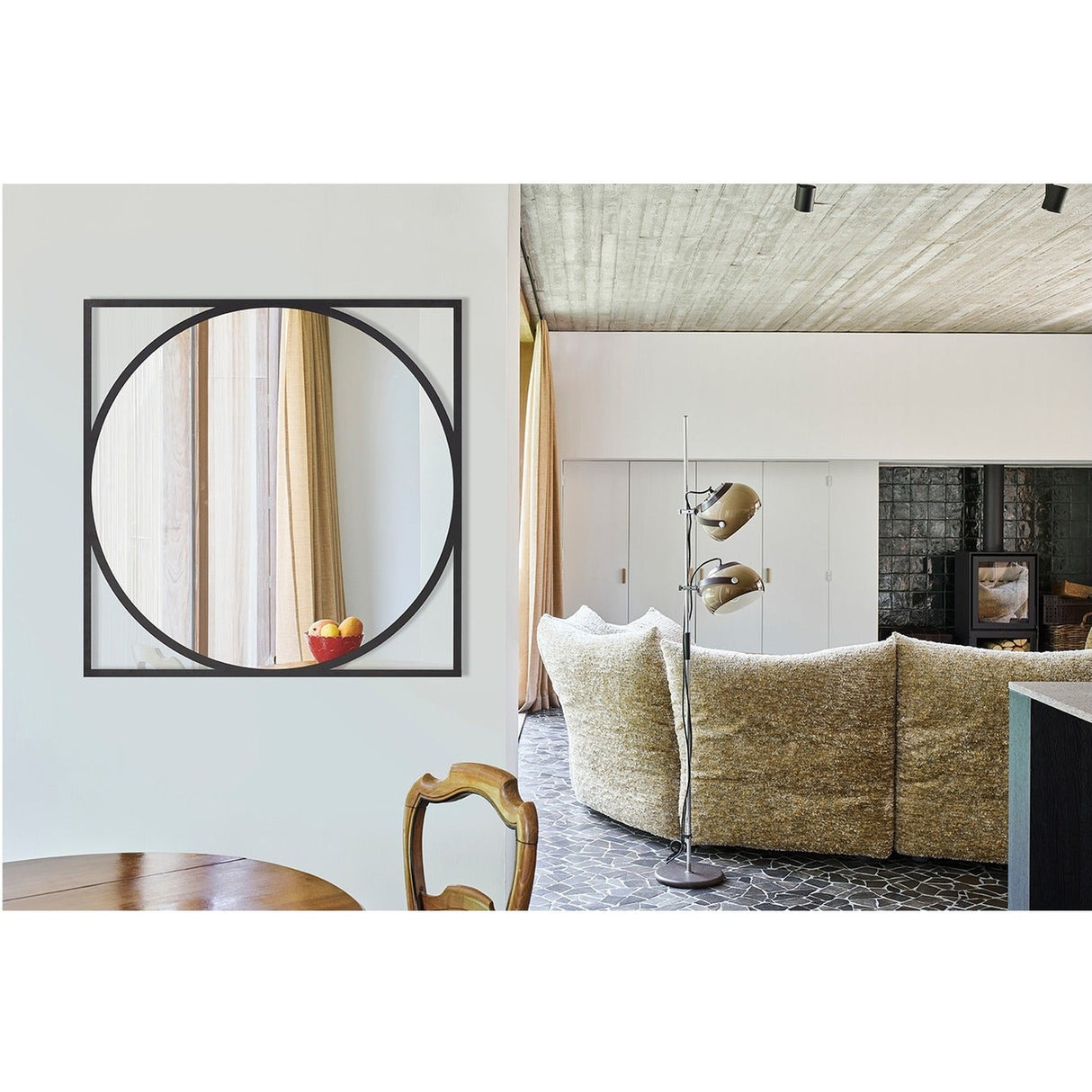 Circo Square Printed Glass Wall Mirror with a black square frame and circular mirrored centre, hung on a light wall in a living room setting.