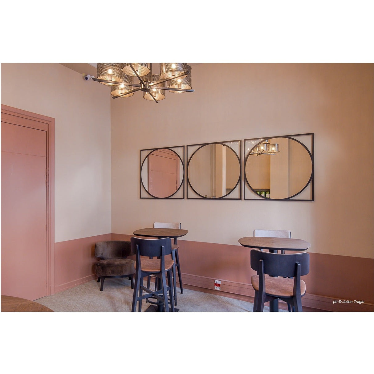 Circo Square Printed Glass Wall Mirror, three black-framed circular panels in a row above a dining area with round tables, dark chairs, and a pink half-painted wall.