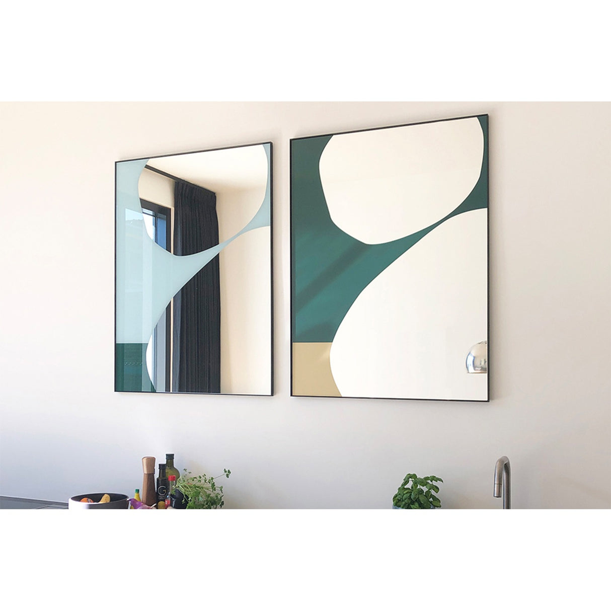 Mika Blue Printed Glass Wall Mirror in a slim black metal frame, shown beside a matching mirror on a wall, with abstract teal, white and sandy curved shapes printed across the lower glass.