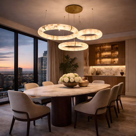 A modern dining room with a marble table, eight upholstered chairs, and sunset city views features the Aureon LED Triple Ring Alabaster Circular Suspension Light – Soft White, adding elegance and warmth to the cozy atmosphere.