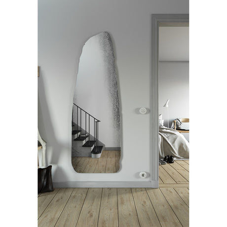 Rocca Standing Stone Printed Glass Wall Mirror 175cm, a frameless irregular mirror shaped like a menhir with a screen-printed stone pattern, mounted in a hallway near a staircase.