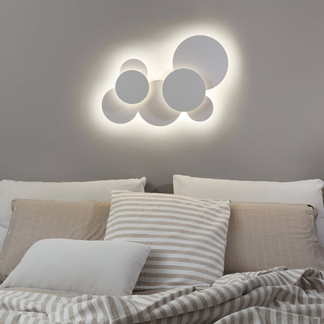 A modern bedroom showcases a gray wall adorned with the Lume LED Semi Flush Light 46W in white, measuring 74cm, which offers energy-efficient lighting and emits a warm 3000K glow. Below, the neatly made bed is dressed in beige and white striped bedding and pillows, establishing a cozy and contemporary ambiance.