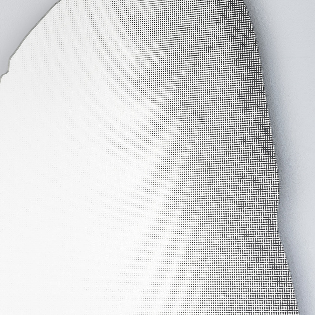 Close-up of the Rocca frameless wall mirror's irregular stone-shaped edge, showing a screen-printed dot gradient in black that creates a shadowed, three-dimensional effect on the glass surface.