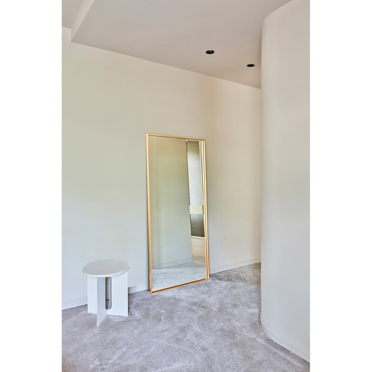 Soho Gold Slim Framed Full Length Mirror 176cm, a rectangular wall mirror with a narrow gold frame, leaning against a wall in a bedroom setting beside a round white side table.