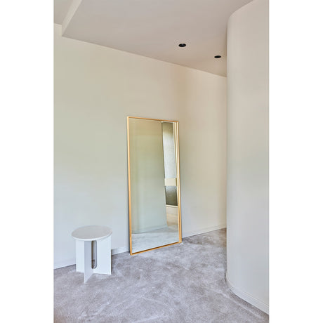 Soho Gold Slim Framed Full Length Mirror 176cm, a rectangular wall mirror with a narrow gold frame, leaning against a wall in a bedroom setting beside a round white side table.