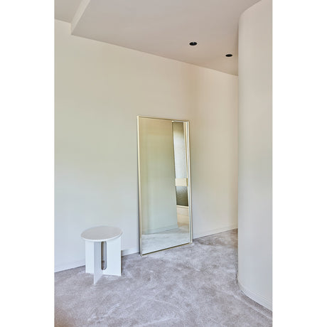 Soho Silver Slim Framed Full Length Mirror 176cm leaning against a light wall in a bedroom, rectangular glass with a narrow flat silver frame, beside a small round white stool.