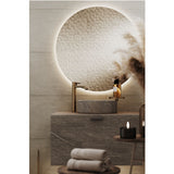 Brio Clear Round LED IP44 Bathroom Mirror above a marble countertop basin, its frameless round glass backlit with a soft ambient glow against the tiled wall.