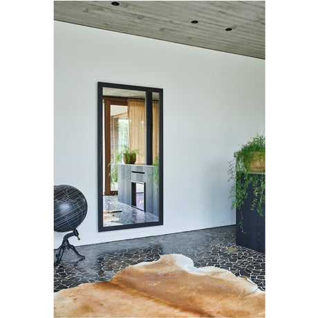 Kyo Wooden Full Length Mirror in Black leans on a white wall in a living room, rectangular black wooden frame reflecting a wood-burning stove and interior view.