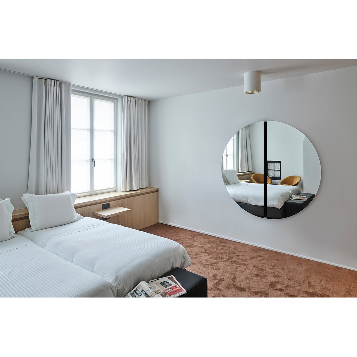 Luna Black Two Piece Round Wall Mirror 150cm above a bed in a bedroom, frameless glass disc split by a black lacquered central strip, reflecting the room.