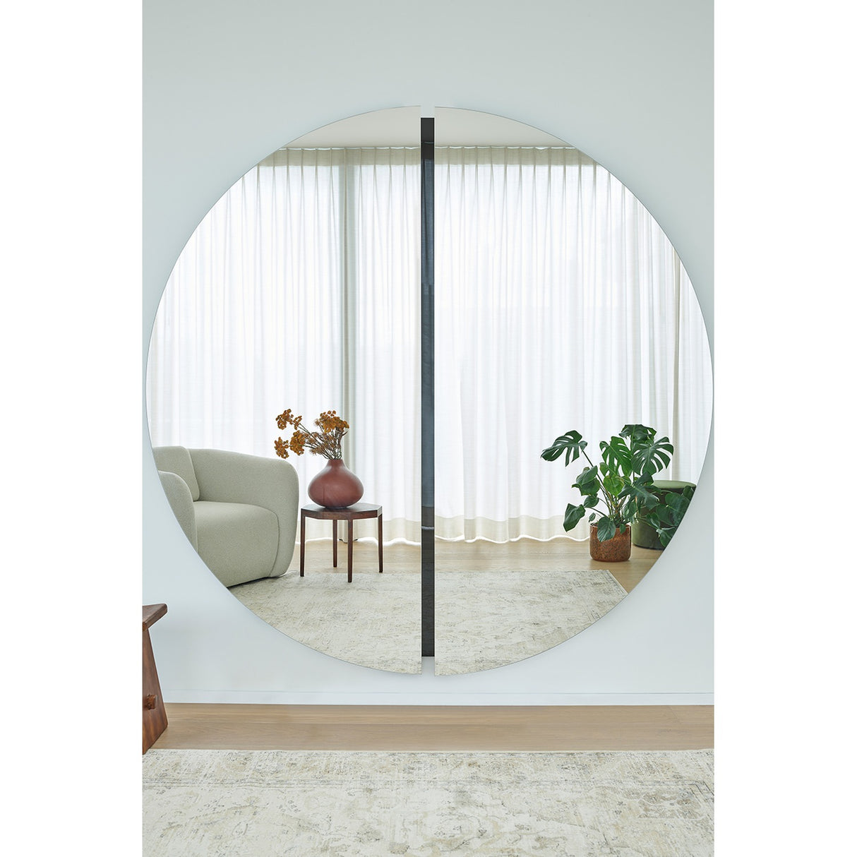 Luna Black Two Piece Round Wall Mirror 200cm, a large frameless round mirror with a black lacquered glass strip at the central join, shown reflecting a bright living room.