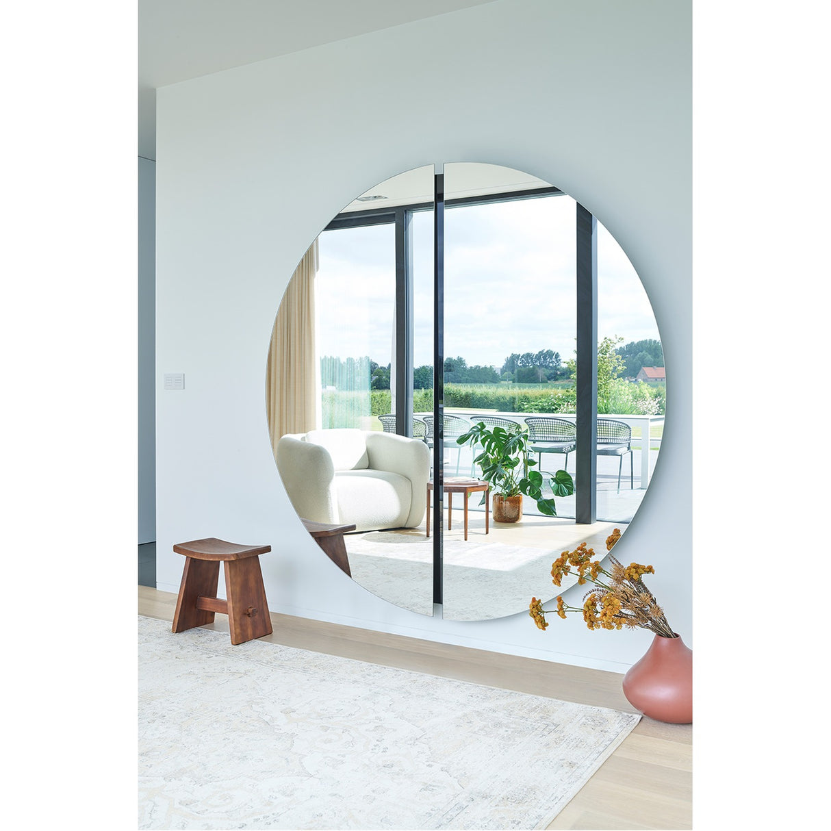 Luna Black Two Piece Round Wall Mirror 200cm, frameless glass with a black lacquered central joint, hung in a living room reflecting a sofa and garden view.