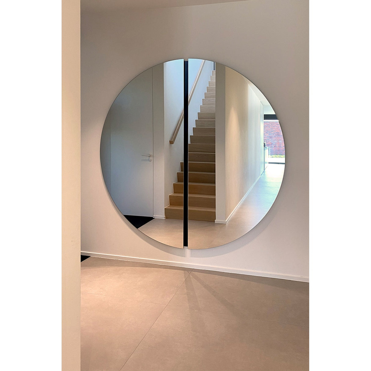Luna Black Two Piece Round Wall Mirror 200cm mounted in a hallway, framed by white walls, reflecting a wooden staircase, with a black lacquered strip marking the central join.
