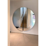 Luna Black Two Piece Round Wall Mirror 200cm mounted in a hallway, framed by white walls, reflecting a wooden staircase, with a black lacquered strip marking the central join.