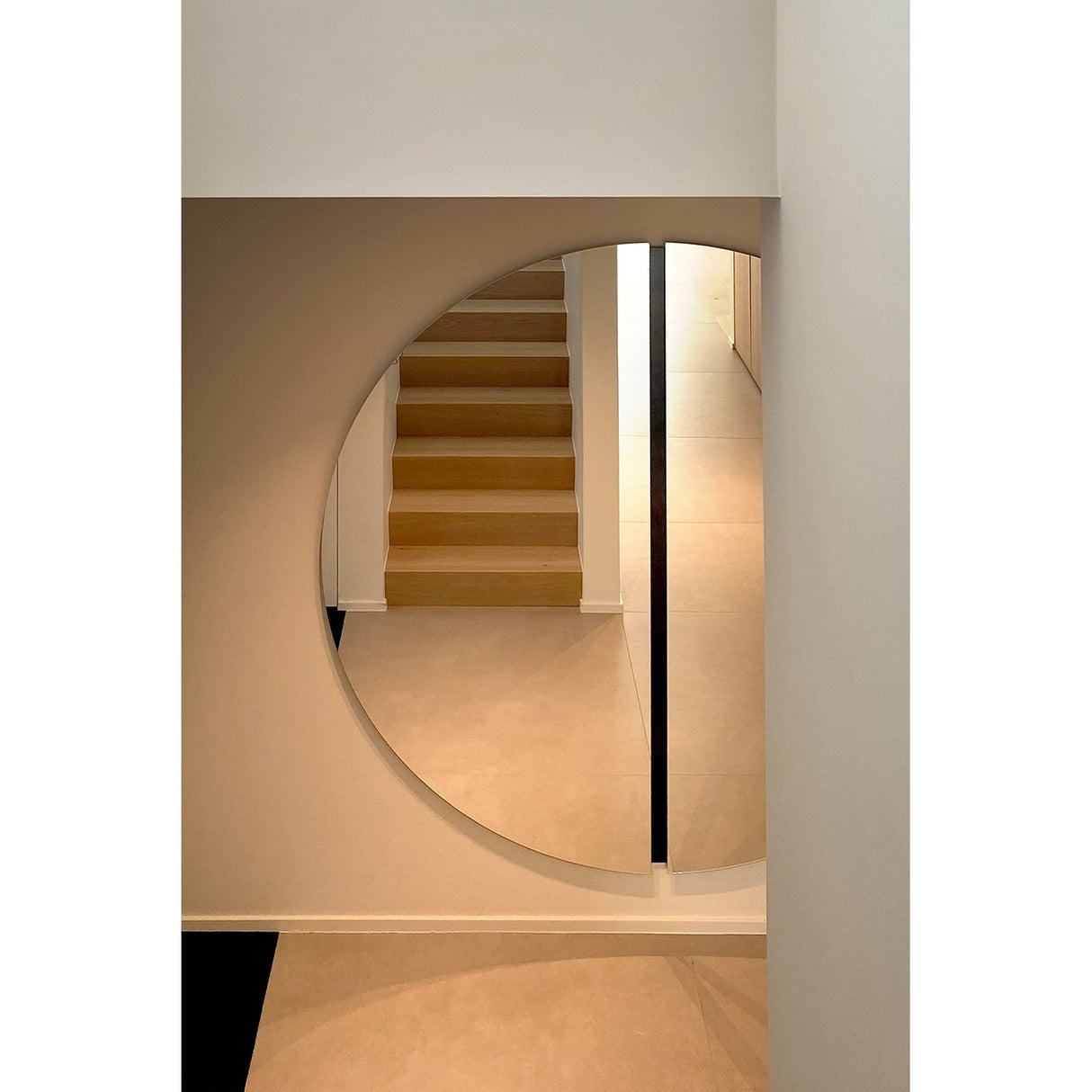 Luna Black Two Piece Round Wall Mirror 200cm reflecting a wooden staircase in a hallway, with a black lacquered glass strip marking the central join between the two frameless round halves.