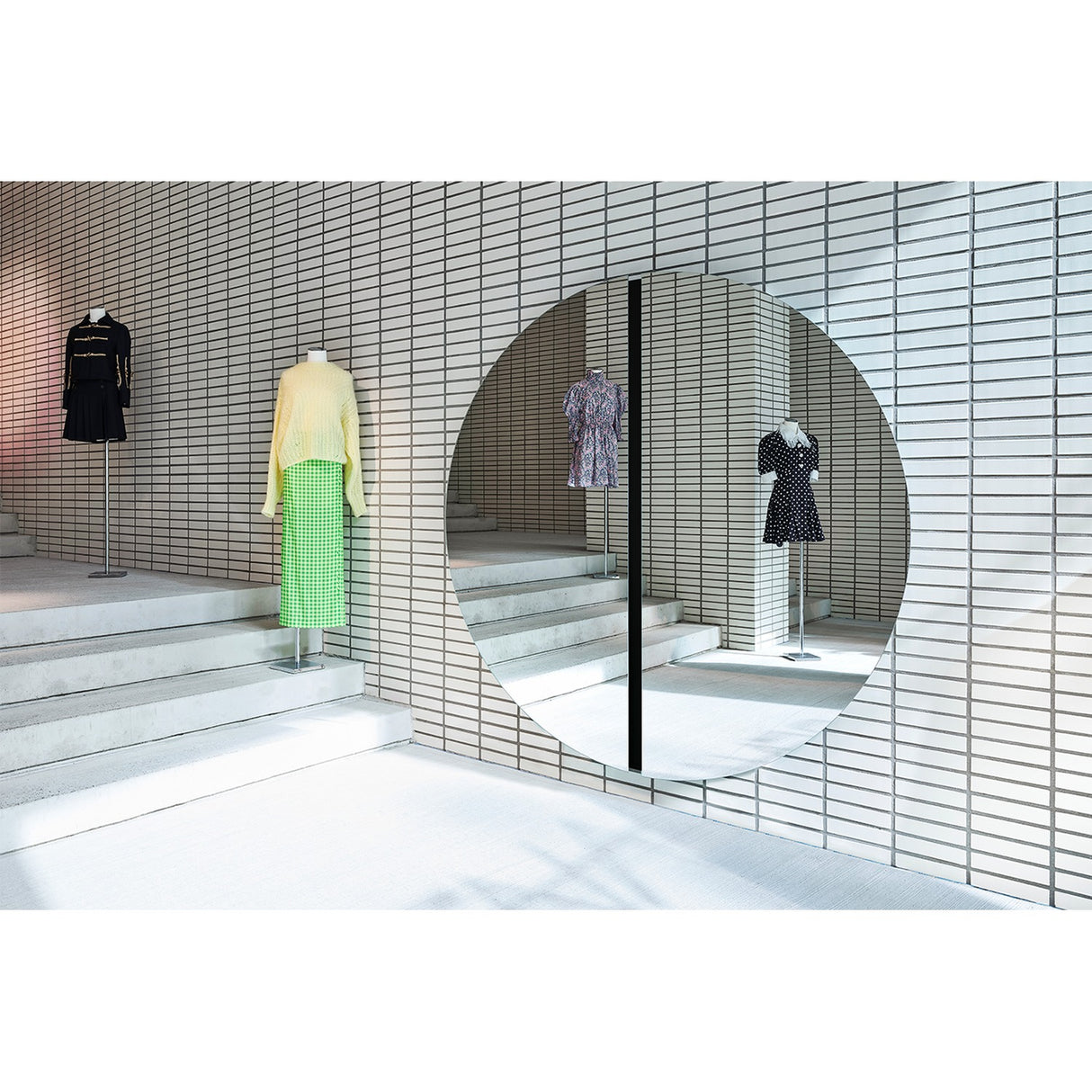 Luna Black Two Piece Round Wall Mirror 200cm mounted on tiled wall in a boutique setting, frameless glass split by a central black lacquered strip, reflecting displayed garments.