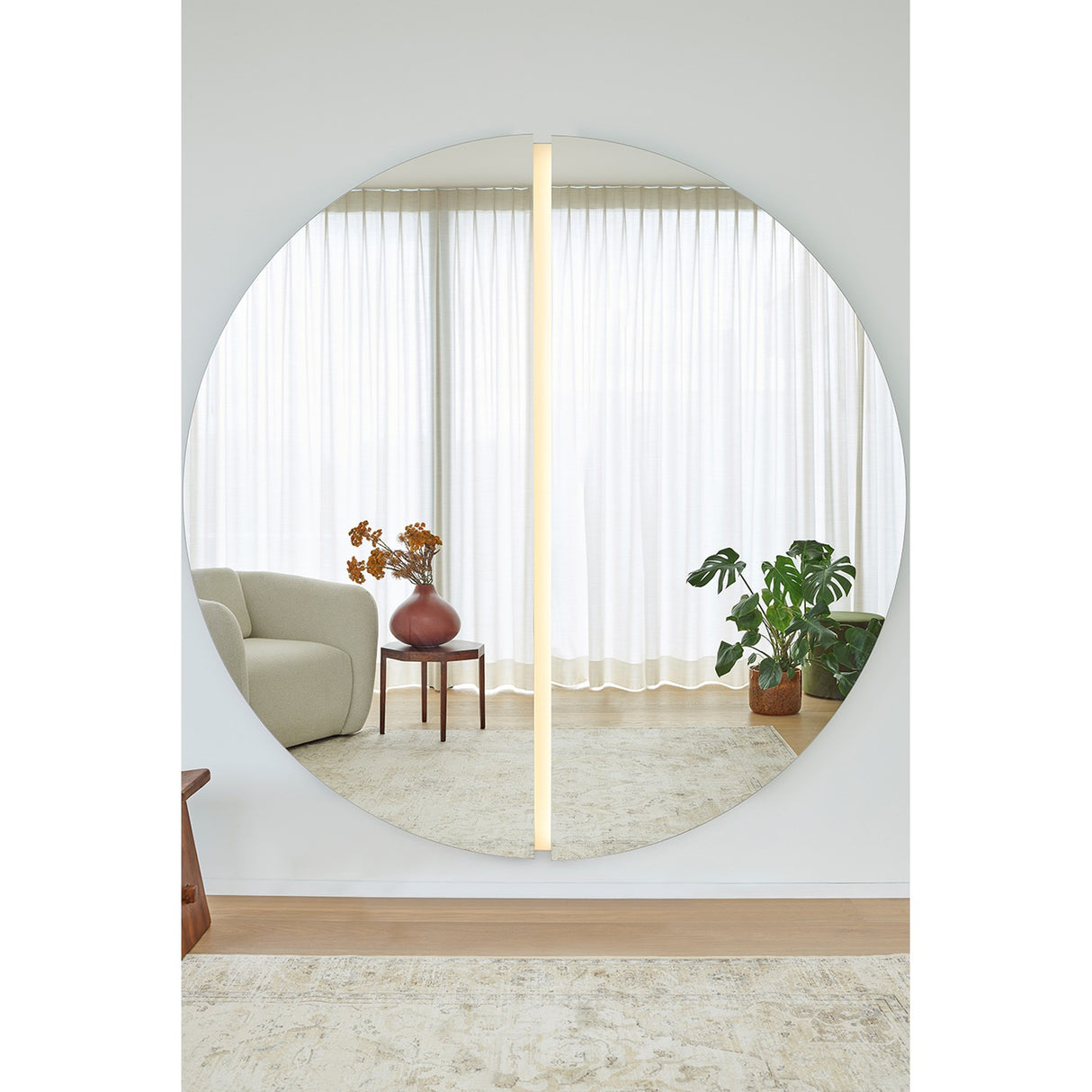 Luna Light LED two-piece round wall mirror, 200cm, frameless glass split into half-moons with a vertical LED strip lighting the central seam, reflecting a living room.