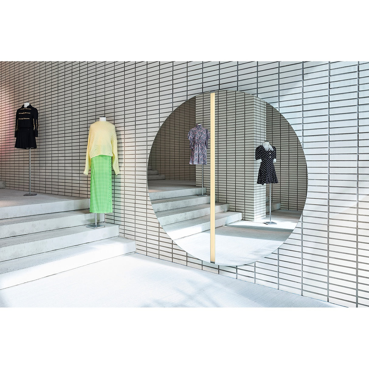 Luna Light LED Two Piece Round Wall Mirror 200cm, a large frameless round mirror with a central LED strip, mounted on a tiled wall reflecting displayed garments in a showroom.