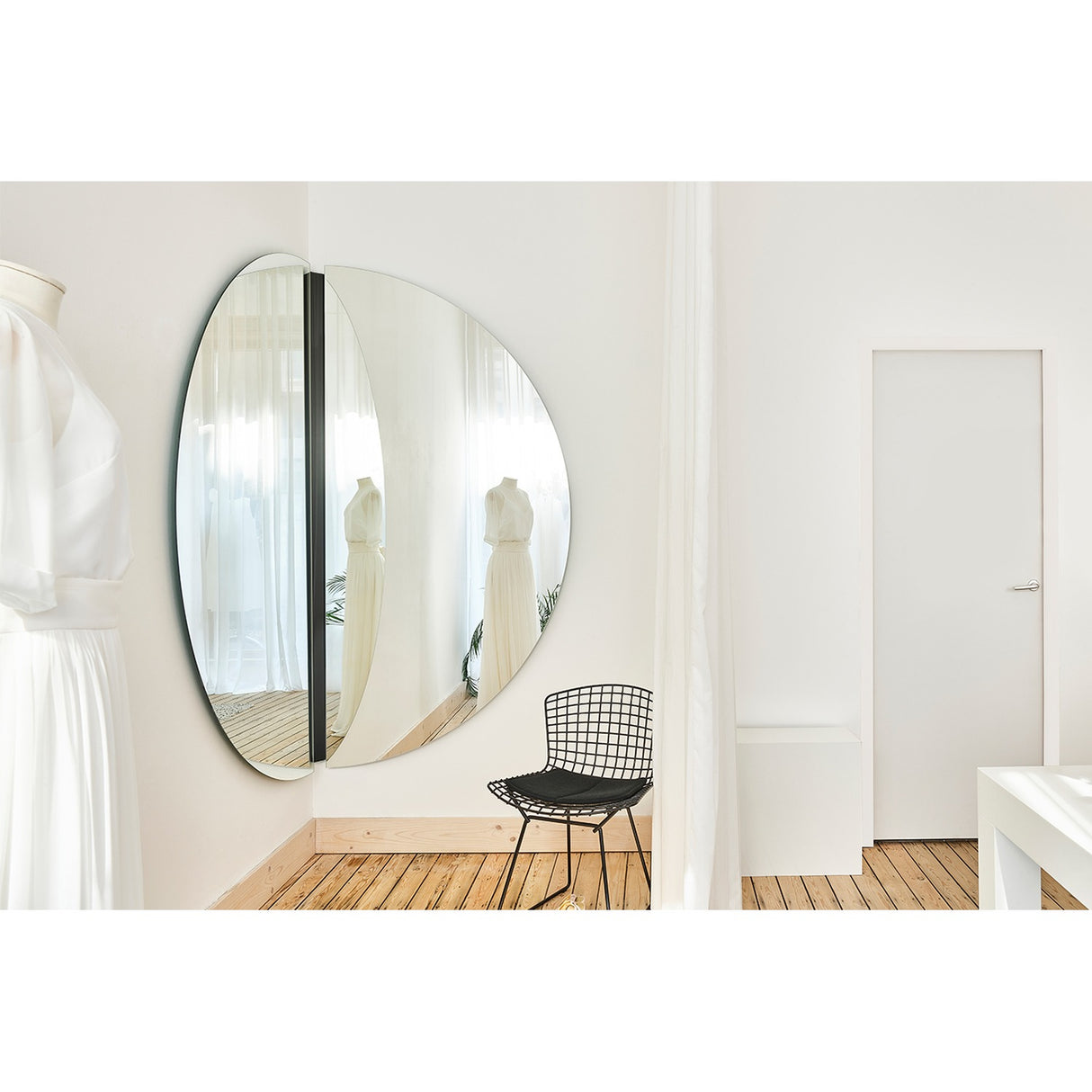Luna Black Two Piece Corner Wall Mirror 200cm, a round frameless glass mirror split into two panels mounted on an external corner, shown in a bright room with a wire chair and hanging dress.