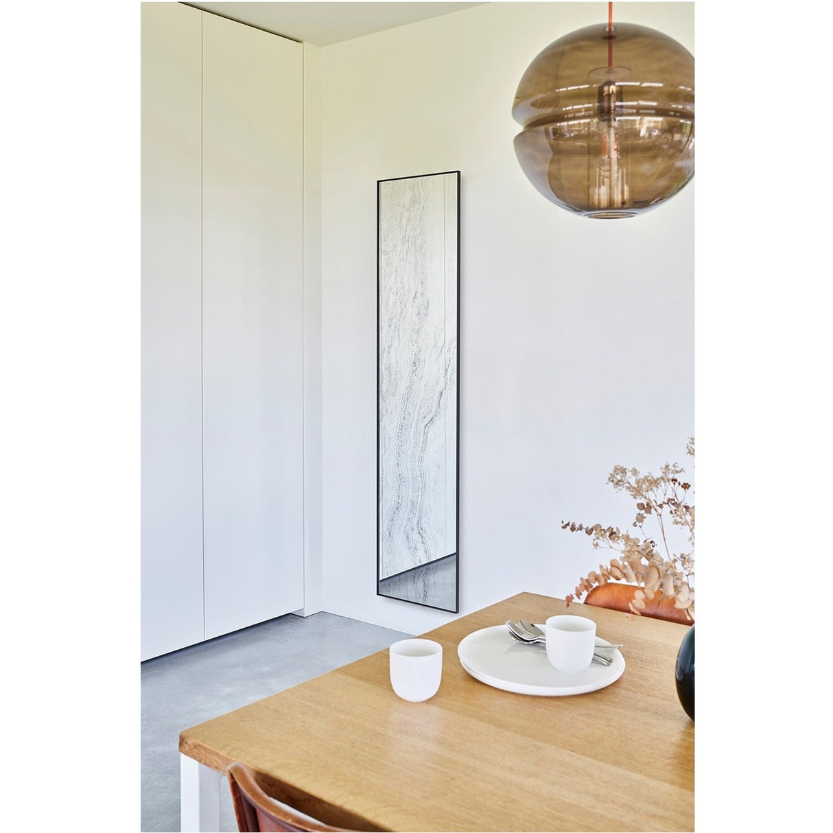 Travertin tall rectangular wall mirror with black metal frame and travertine-print glass, mounted in a corner hallway near a dining table and pendant light.