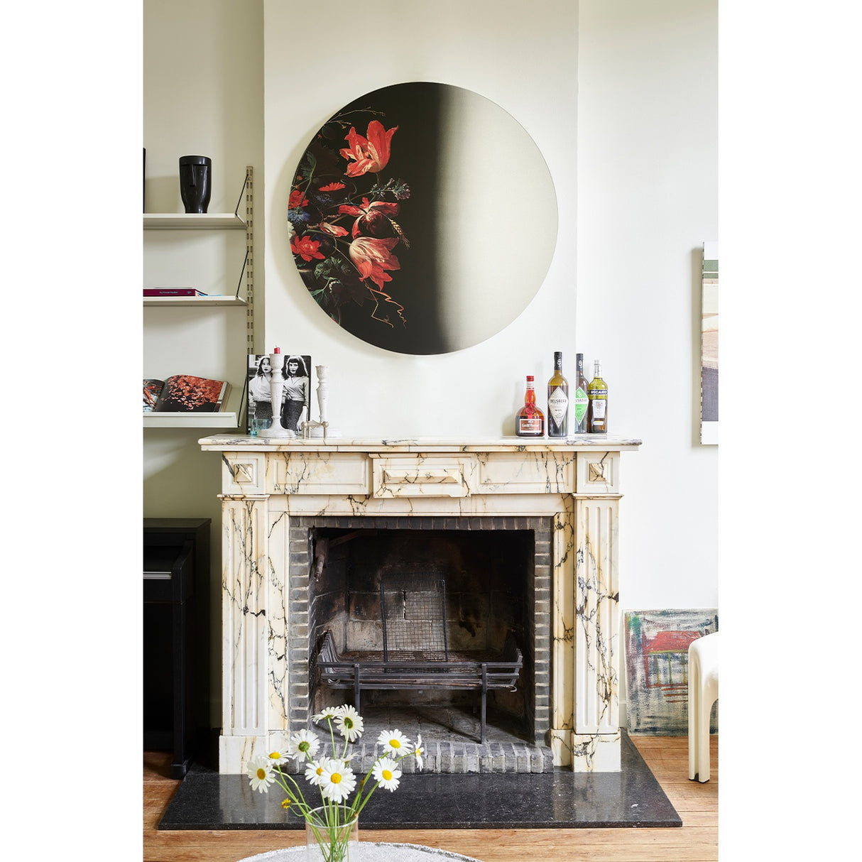 Museo Still Life Printed Round Wall Mirror 100cm, frameless glass mirror with a printed floral still-life fragment on one side, mounted above a marble fireplace in a living room.