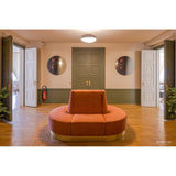 Museo Still Life Printed Round Wall Mirror 100cm, a frameless circular mirror with a dark floral still-life print, shown either side of a green panelled door in a hallway with orange curved sofa.