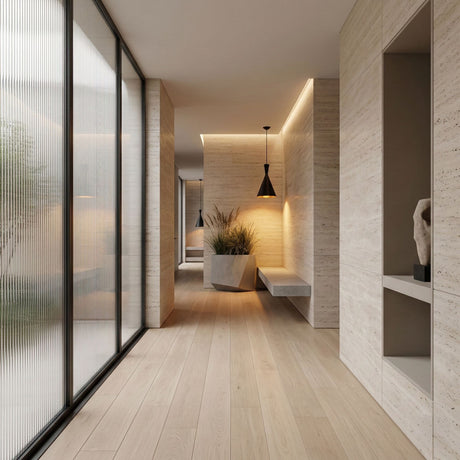 A modern, minimalist hallway features light wood floors, beige textured walls, built-in shelving, frosted glass panels, a bench with a large planter, sleek modern lighting, and is illuminated by the Funk Tall Pendant Light - Black. Natural light fills the space.