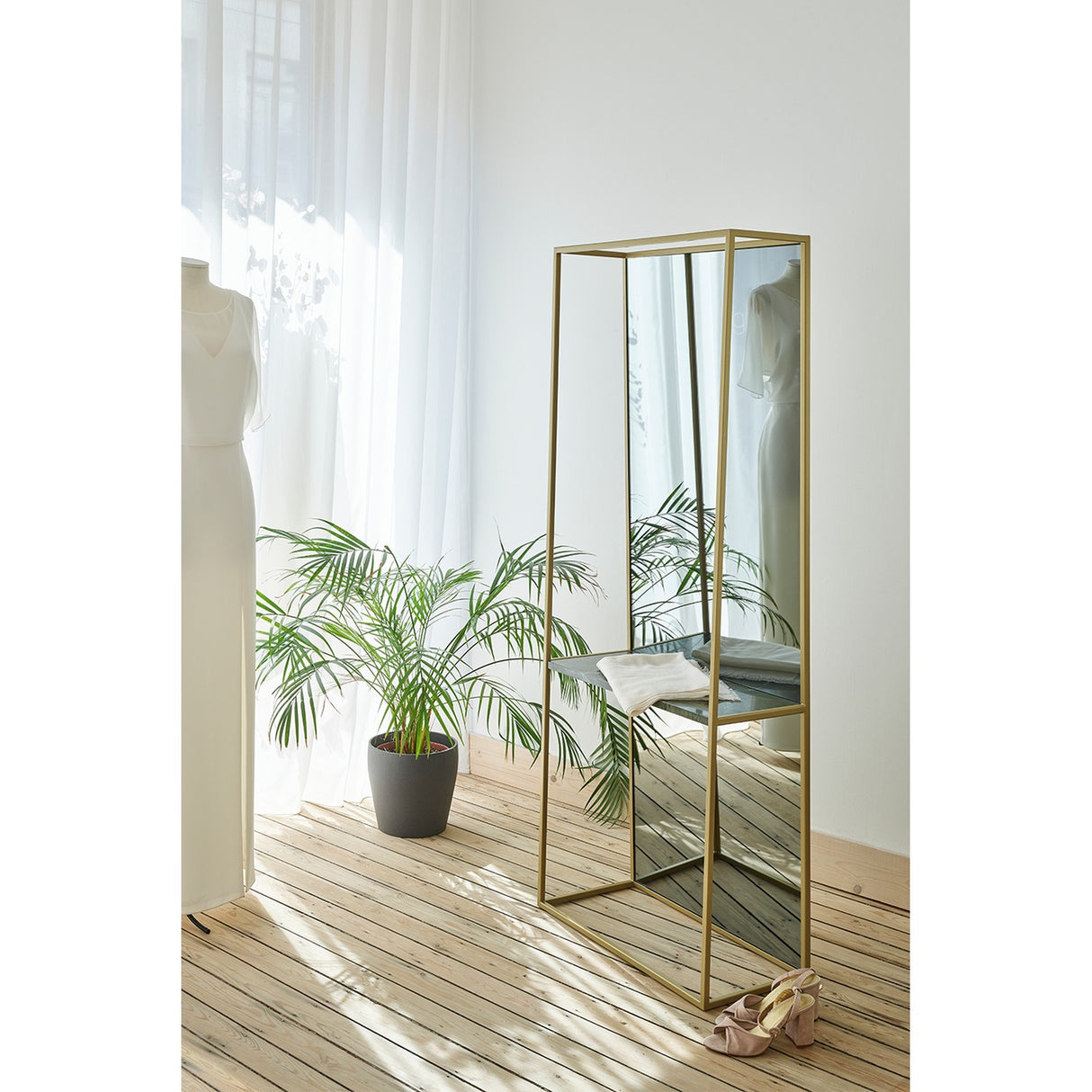 Chassis XL Deluxe free standing cheval mirror in a gold metal frame with a green marble shelf, shown in a bedroom beside a plant and mannequin.