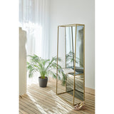 Chassis XL Deluxe free standing cheval mirror in a gold metal frame with a green marble shelf, shown in a bedroom beside a plant and mannequin.
