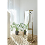 Chassis XL Deluxe free standing cheval mirror in a gold open metal frame with a marble shelf, styled in a bedroom holding a hanger with clothing beside a plant and sheer curtains.