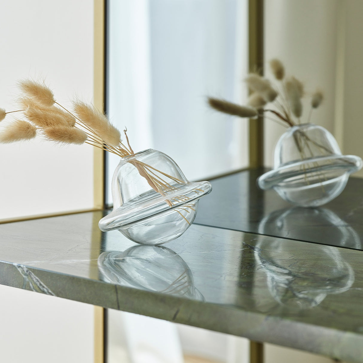 Close-up of the Chassis XL Deluxe free standing mirror's green marble shelf with gold metal frame, holding a clear glass vase with dried grass, reflected in the mirror.