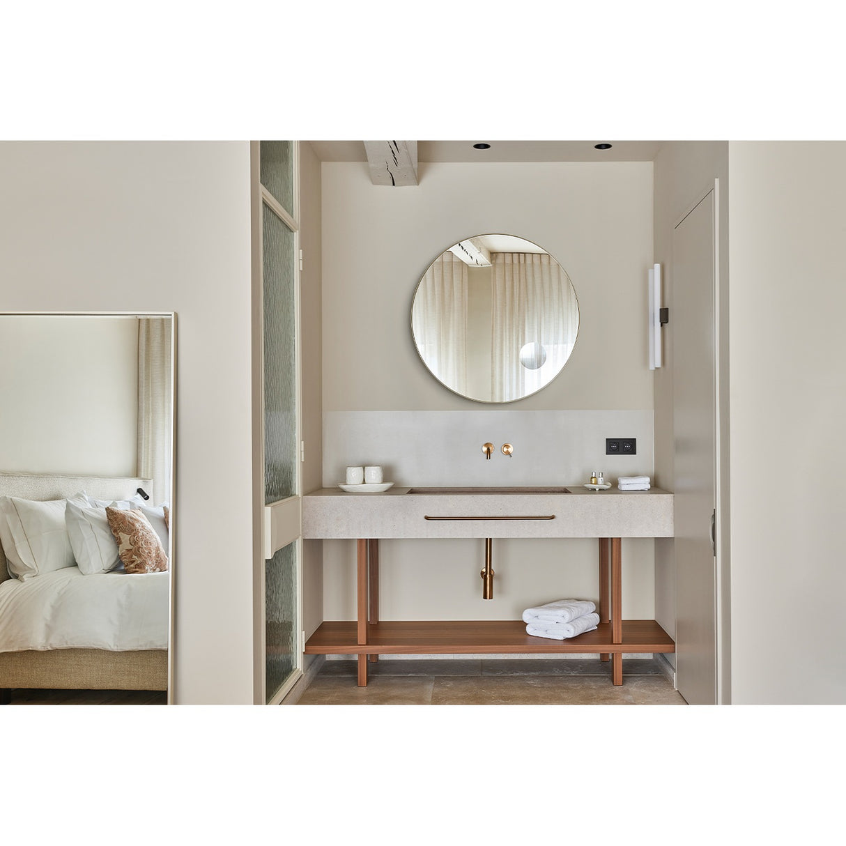 Hoop Zoom Bronze round wall mirror, 85cm, with built-in magnifying section, shown above a bathroom vanity with brass tap fittings and wooden shelving.