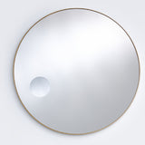 The bronze framed round mirror seen larger, the magnifying circle reading low and to one side of the face.