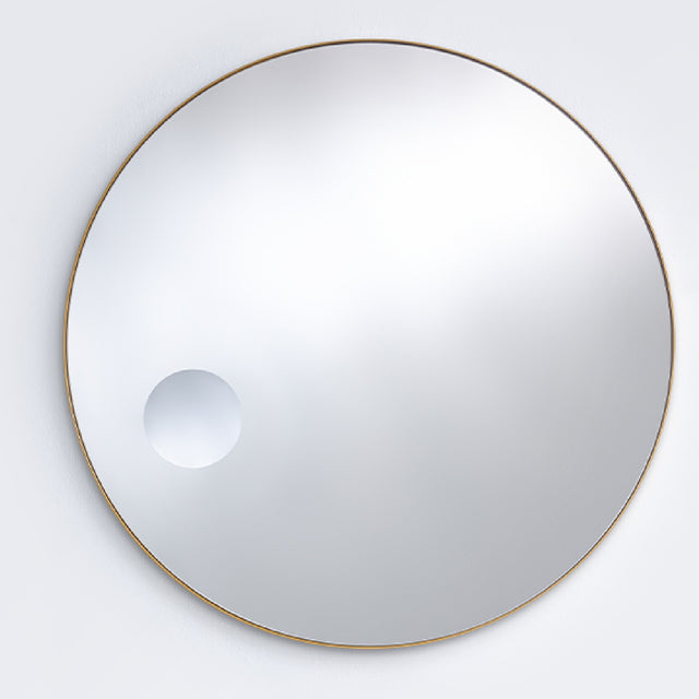 The bronze framed round mirror seen larger, the magnifying circle reading low and to one side of the face.