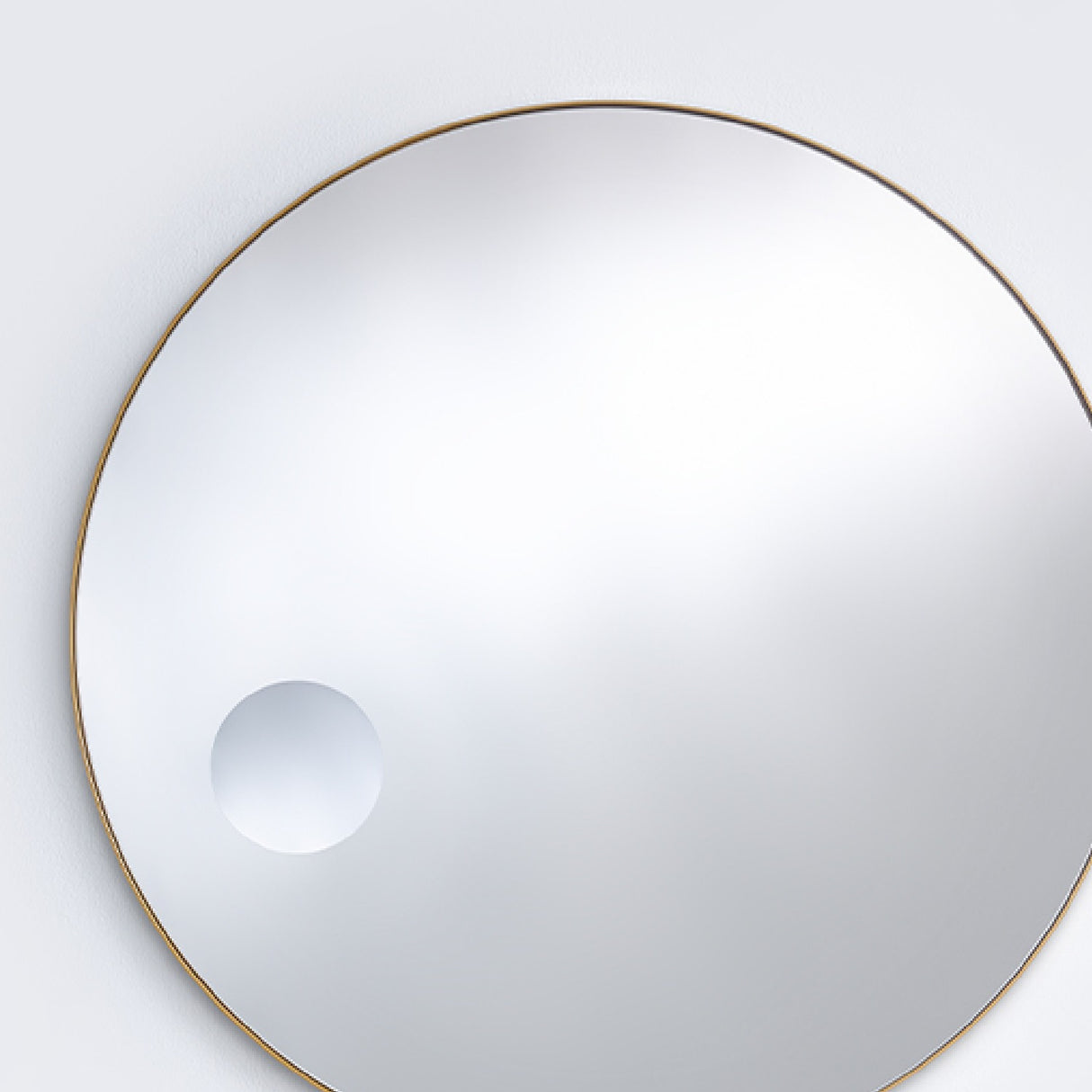 The bronze framed round mirror seen larger, the magnifying circle reading low and to one side of the face.