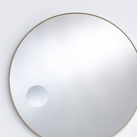The bronze framed round mirror seen larger, the magnifying circle reading low and to one side of the face.