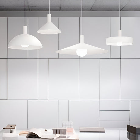 A modern office space is accented by four Arion 1 Light Pendants in white, elegantly hanging from the ceiling. The background highlights sleek, white geometric wall panels, while the desk below is adorned with open books, papers, and neatly stacked small boxes. Ideal for those who value minimalist lighting in their decor.