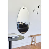 Globo Lago Oak Peg Hung Wall Mirror, a frameless organic-shaped 122cm mirror with a facetted edge, hung from a solid oak peg in a hallway above a bench and round table.