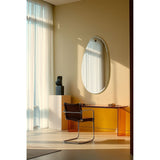 Globo Lago Oak Peg Hung Wall Mirror, an oval frameless mirror on a wooden peg, shown above a glass console table in a sunlit living room setting.