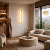 A modern living room with neutral tones features a round beige coffee table, light sofas, sculptural floor lamp, built-in shelving, and the Averra LED Large Round Alabaster Wall Light in Soft White & Brass illuminating the space.
