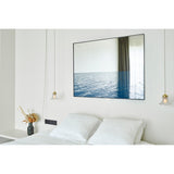 Maro Seascape Printed Glass Wall Mirror 120cm in a black rectangular frame above a bed, with a mirrored upper half and printed blue seascape across the lower section.